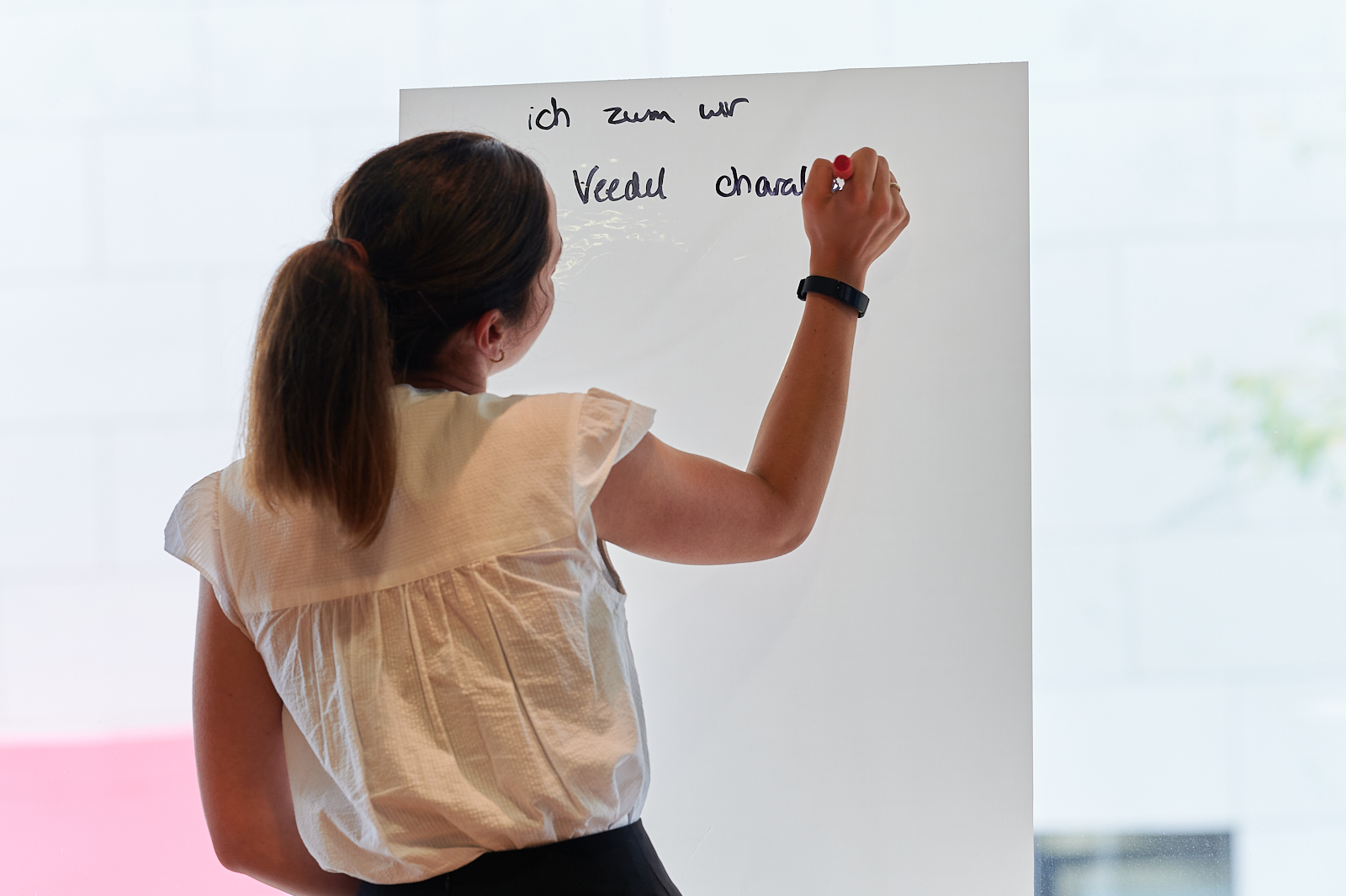 Frau steht mit dem Rücken zur Kamera und schreibt auf ein Flipchart
