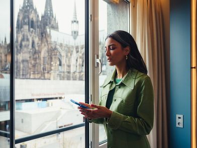 Eine Geschäftsreisende steht am Hotelfenster mit Blick auf den Kölner Dom