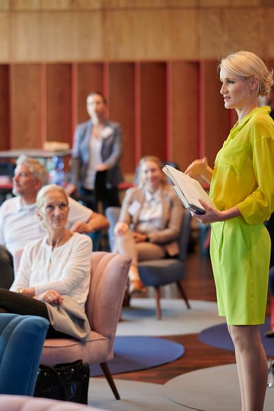 Rednerin steht in der Mitte zwischen dem sitzenden Publikum