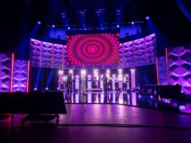 Bühnenperformance: Eine Band steht auf einer lila und pink beleuchteten Bühne mit großen bespielten LED Leinwänden im Hintergrund