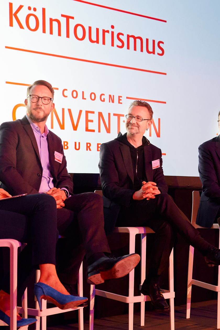 Vier Personen sitzen auf Barstühlen auf einer Bühne und führen eine Podiumsdiskussion