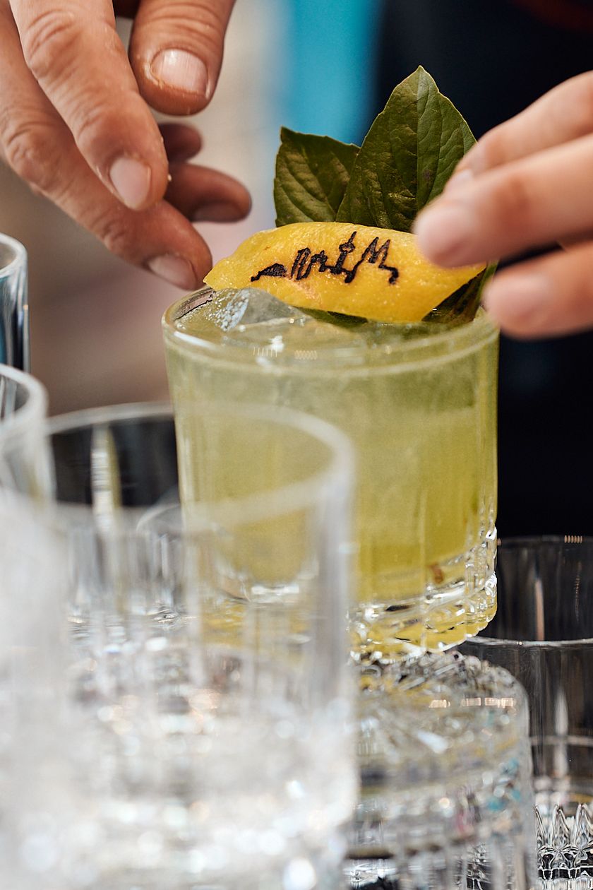 Nahaufnahme: Cocktail mit Zitronenschale auf der die Kölner Skyline eingraviert ist