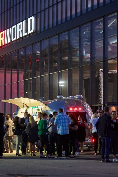 Motorworld Köln von außen. Vor der großen Halle stehen Menschen, die sich unterhalten.