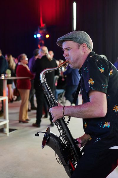 Saxophonist spielt, im Hintergrund stehen Personen