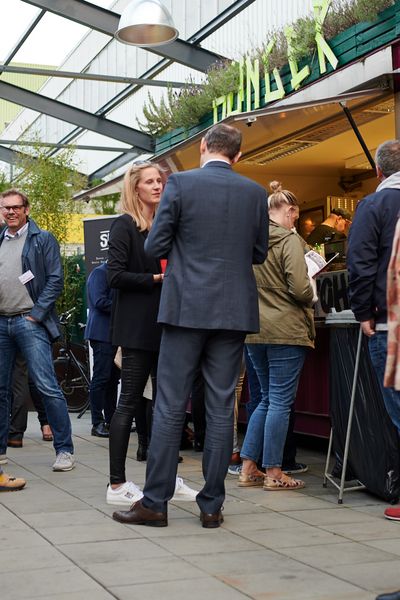 Menschen unterhalten sich im Außenbereich vor Foodtrucks