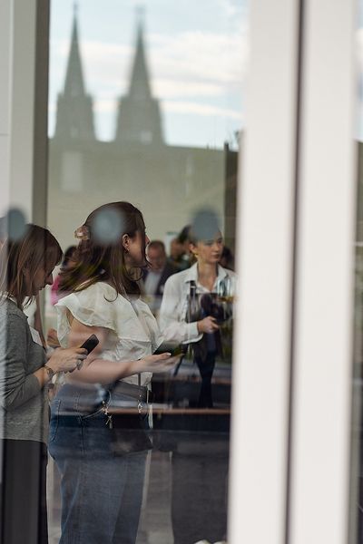 Tür von außen fotografiert, im Glas spiegelt sich der Kölner Dom und im Inneren sind die Gäste der Veranstaltaltung zu sehen