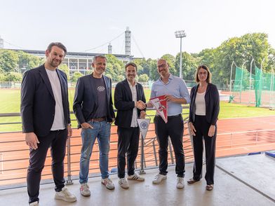 5 Personen der Deutschen Sporthochschule und des 1. FC Köln stehen im RheinEnergie Stadion in einer Reihe, um die Kooperation beider Unternehmen zu feiern.