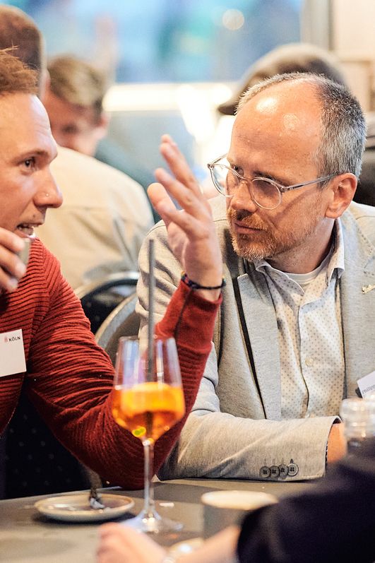 Zwei Männer sitzen bei einem Drink am Tisch und unterhalten sich