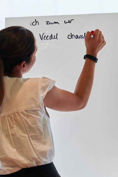 Frau steht mit dem Rücken zur Kamera und schreibt auf ein Flipchart