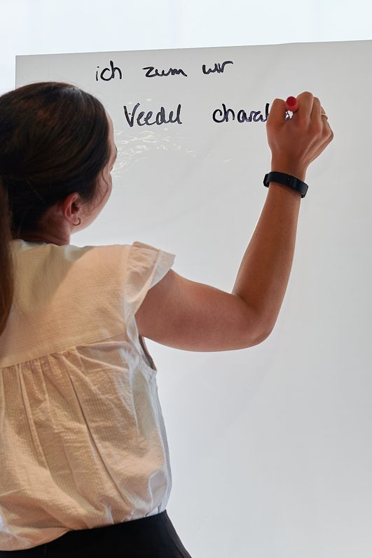 Frau steht mit dem Rücken zur Kamera und schreibt auf ein Flipchart