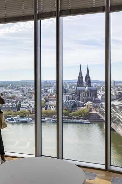 Zwei Frauen schauen aus dem KölnSky Panoramafenster von oben auf die Kölner Skyline mit Rhein, Hohenzollerbrücke und Dom