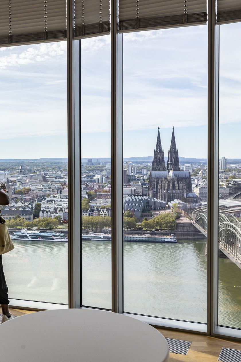 Zwei Frauen schauen aus dem KölnSky Panoramafenster von oben auf die Kölner Skyline mit Rhein, Hohenzollerbrücke und Dom