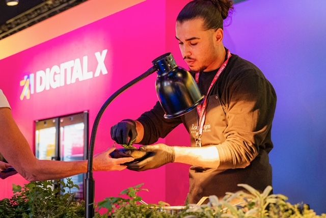 Nachhaltiges Catering auf der digital X: Ein Mann bereitet das Essen vor einem pinken digital X Stand vor.