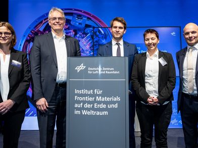 Enthüllung des neuen Institutschilds Frontier Materials in Köln. 5 Personen in Anzügen und Kostüm stehen um das Schild herum.