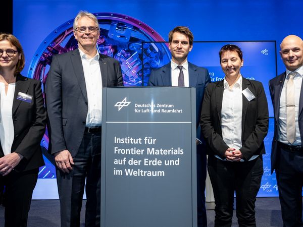 Enthüllung des neuen Institutschilds Frontier Materials in Köln. 5 Personen in Anzügen und Kostüm stehen um das Schild herum.