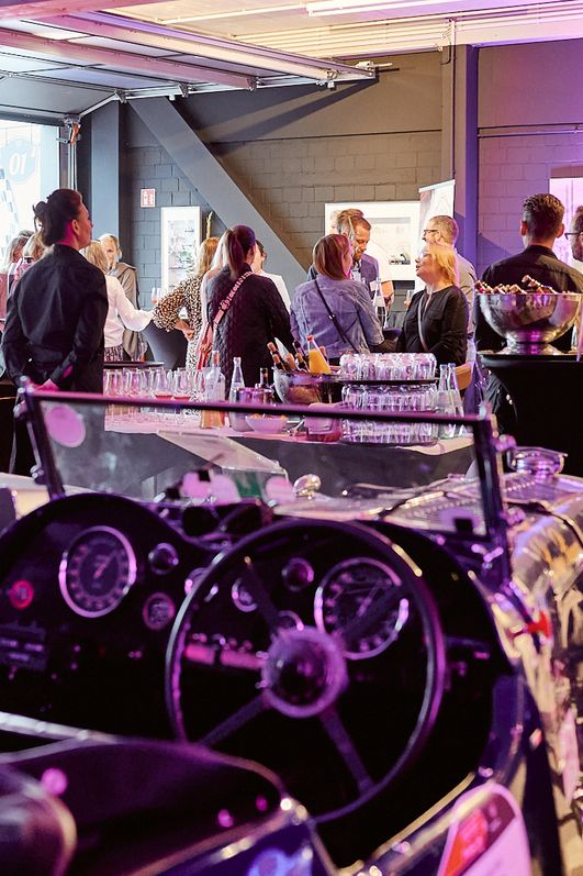 Veranstaltungsgäste unterhalten sich, im Vordergrund steht ein Oldtimer