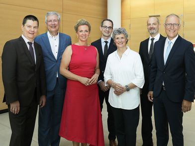 Sieben Menschen stehen in Anzug und Kleid gekleidet in einer Reihe