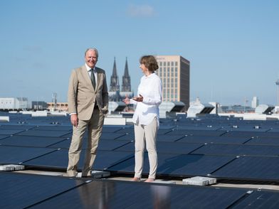 Geschäftsführer der Koelnmesse und die Oberbürgermeisterin Kölns stehen auf dem Dach der Koelnmesse zwischen zahlreichen Solar-Panels zur Einweihung der größten Innerstädtischen Solaranlage Kölns
